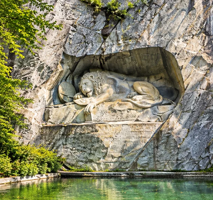 The Lion Monument carved into a sandstone cliff above a still pond